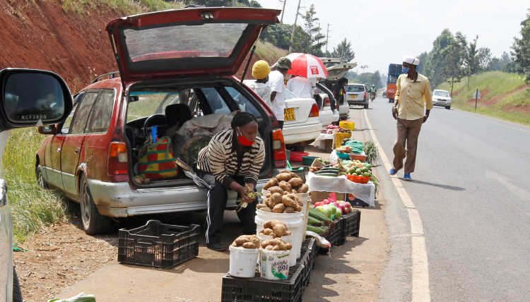 Woman wearing a mask sitting in her car, selling vegetabel nearby a road.