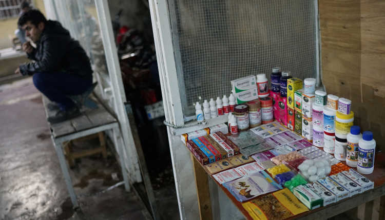 A man is sitting in front of a street stall with medicine.