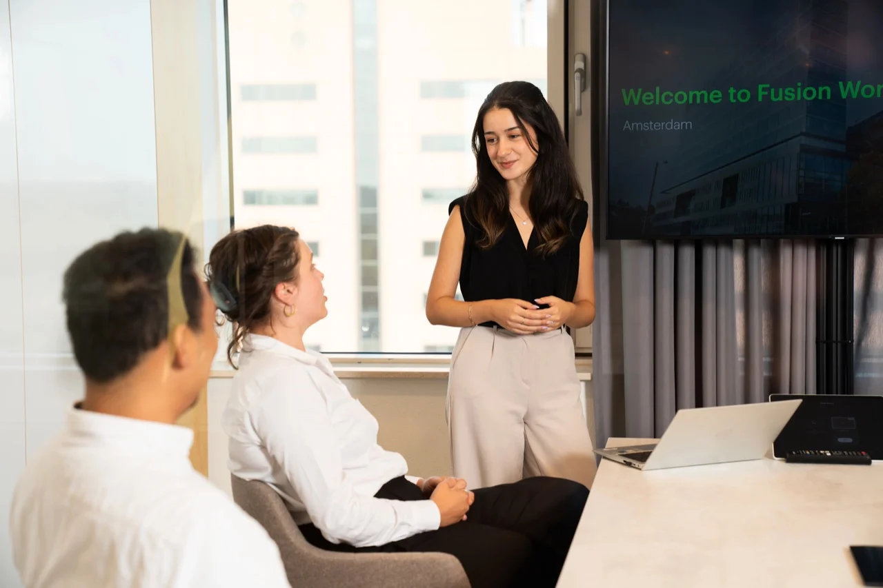 A Fusion Worldwide employee presenting to colleagues in a meeting room.