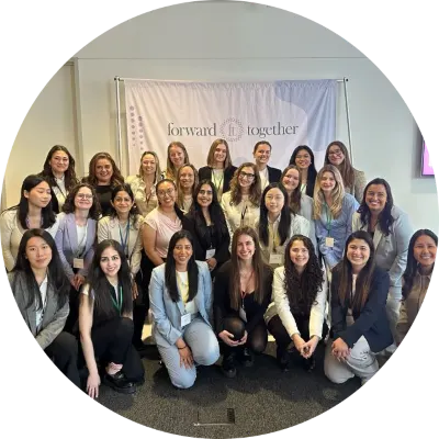 Un grand groupe de femmes pose ensemble en souriant devant une bannière affichant « forward together » lors d’un événement intérieur