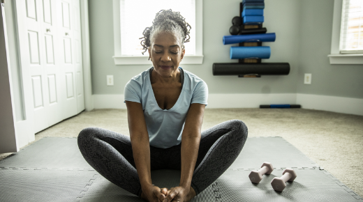 Woman sitting on a mat and stretching next to a set of weights.