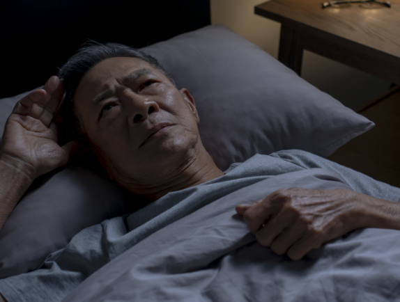 Man experiencing sleeplessness awake in bed.