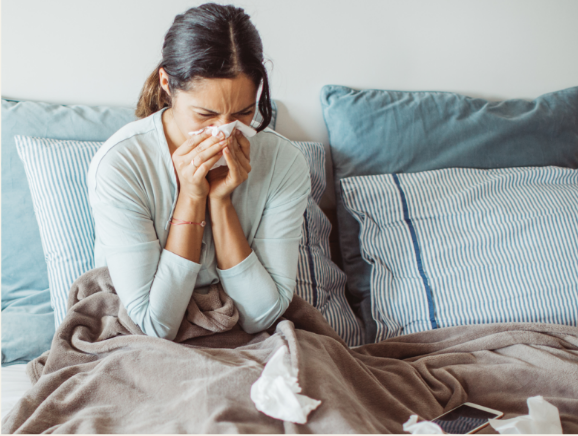 Woman with a cold blowing her nose in bed.