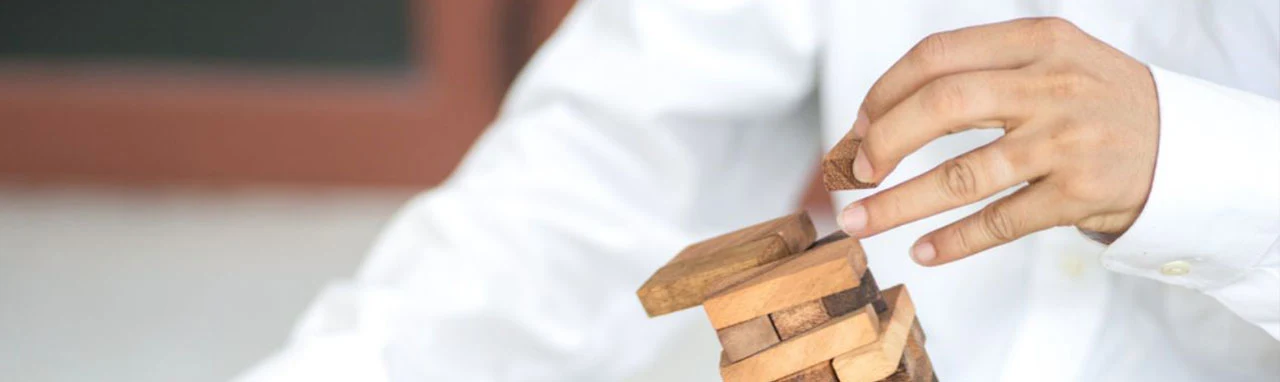 Un homme en chemise fait tombé une pyramide de morceau de bois