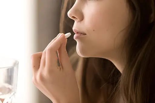 Un visage de femme, elle tient un verre d'eau dans un main et un médicament dans l'autre
