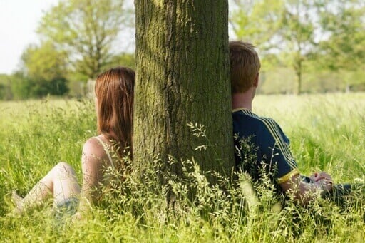 Un couple s'appuie sur un arbre. Ils regardent dans une position opposé