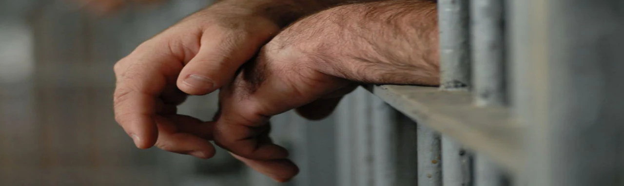 Gros plan sur les mains d'un homme qui dépasse d'une cellule de prison