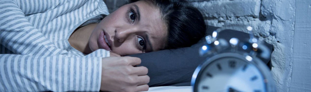 Une femme est allongé dans un lit devant un réveil indiquant 4h du matin