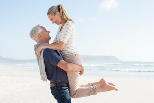 Un couple agé mais dynamique. L'homme porte un tee-shirt bleu, ils se regardent l'un l'autre. On peut voir la mer en fond