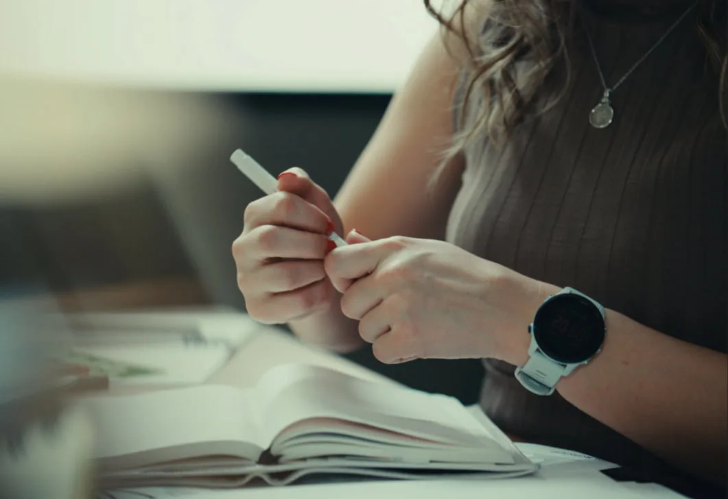 Kailey holds a pen in hand with a notebook on her desk in front of her.