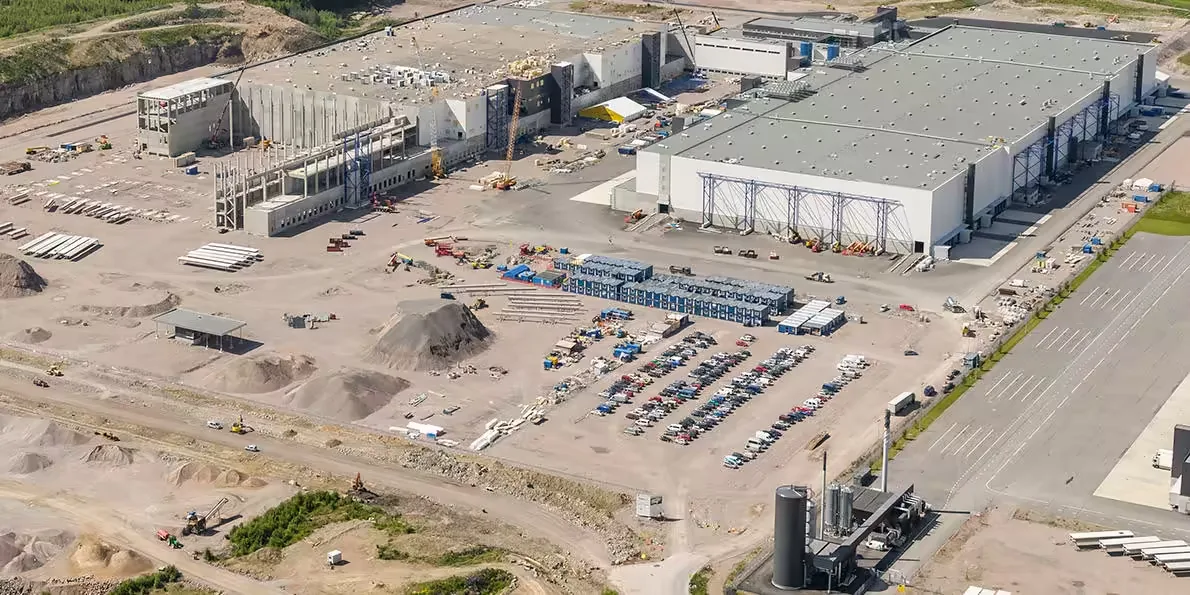 Aerial view of a large industrial site with multiple buildings under construction, cranes, vehicles, and piles of materials.