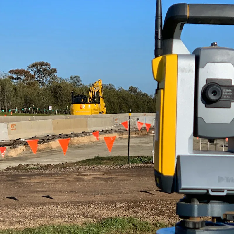 Surveying equipment at a construction site with an excavator in the background.