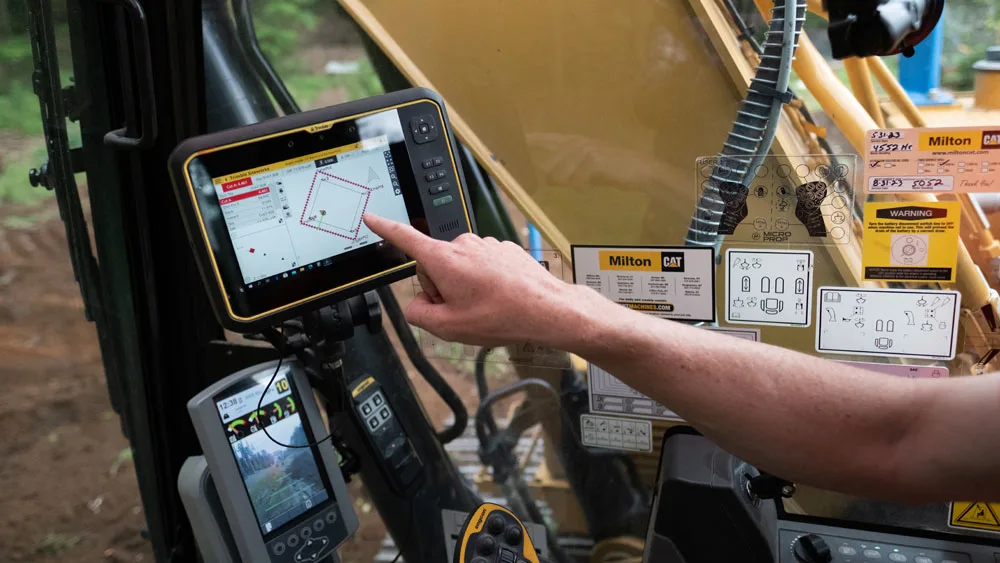 Operator uses touchscreen display with GPS map and controls inside heavy machinery cab.