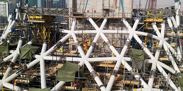 Workers construct a futuristic white star-shaped structure on a building site.