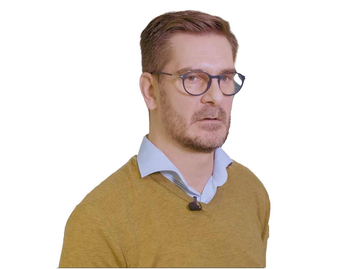 A man with short brown hair, glasses, a light blue collared shirt, and a mustard yellow sweater is shown from the chest up.