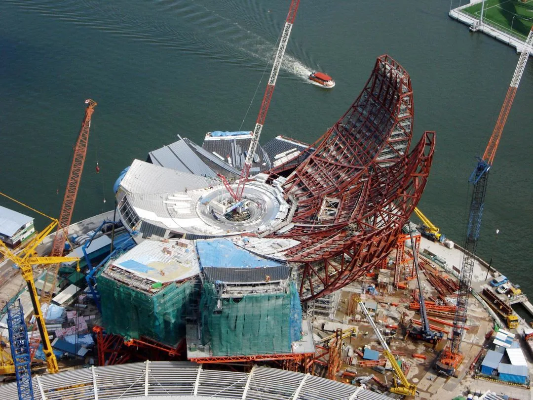 Aerial view of the ArtScience Museum under construction in Singapore, with cranes and scaffolding around the building.