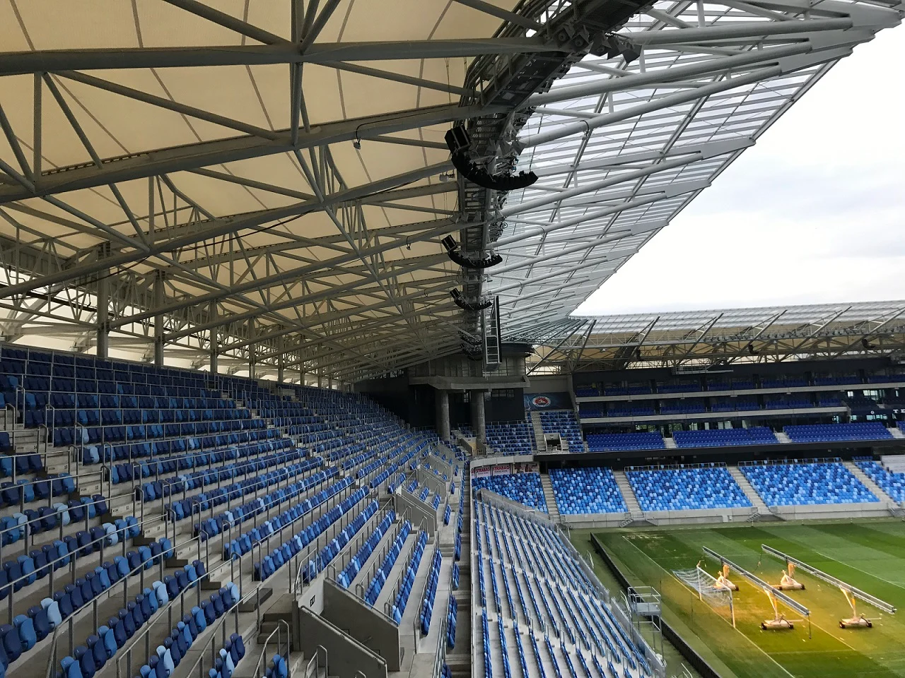 Empty stadium seats with a view of the soccer field and roof structure.