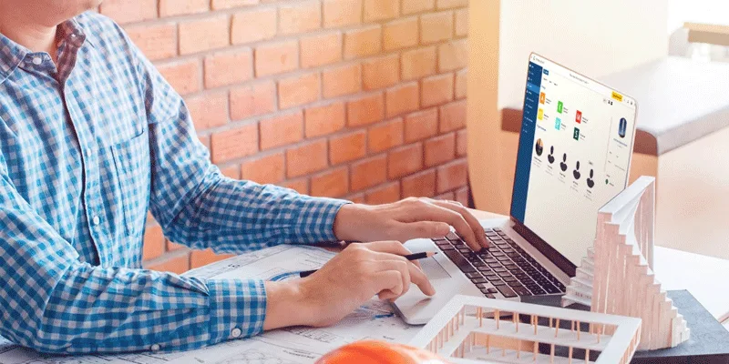 Architect working on a laptop with blueprints and architectural models on desk.