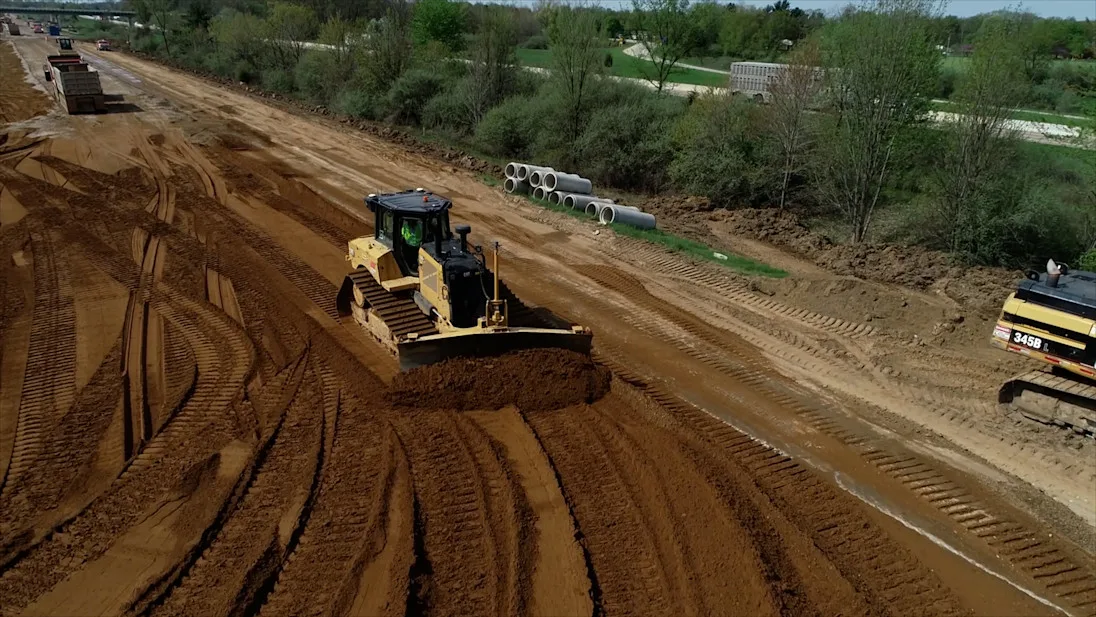 A bulldozer levels earth at a construction site, leaving behind tire tracks.
