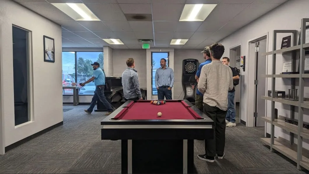 Employees enjoy recreation in a break room with a pool table and dartboard.