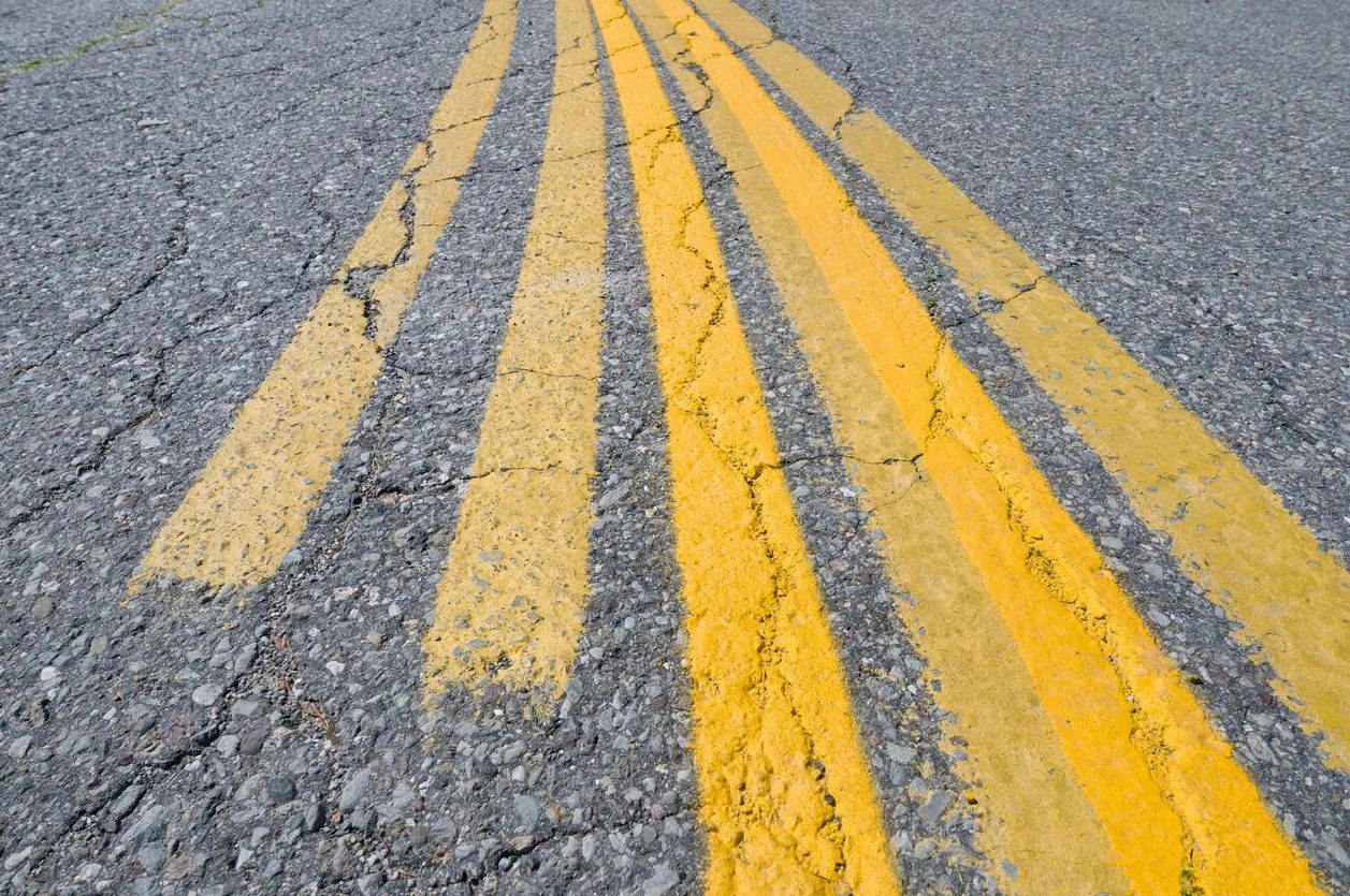 Close-up of double yellow lines painted on a cracked asphalt road.