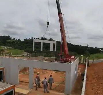 A large red crane lifts a precast concrete wall panel into place at a construction site, where workers are assembling a new building.