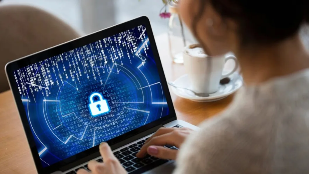 A person types on a laptop displaying a digital padlock and binary code, symbolizing cybersecurity.