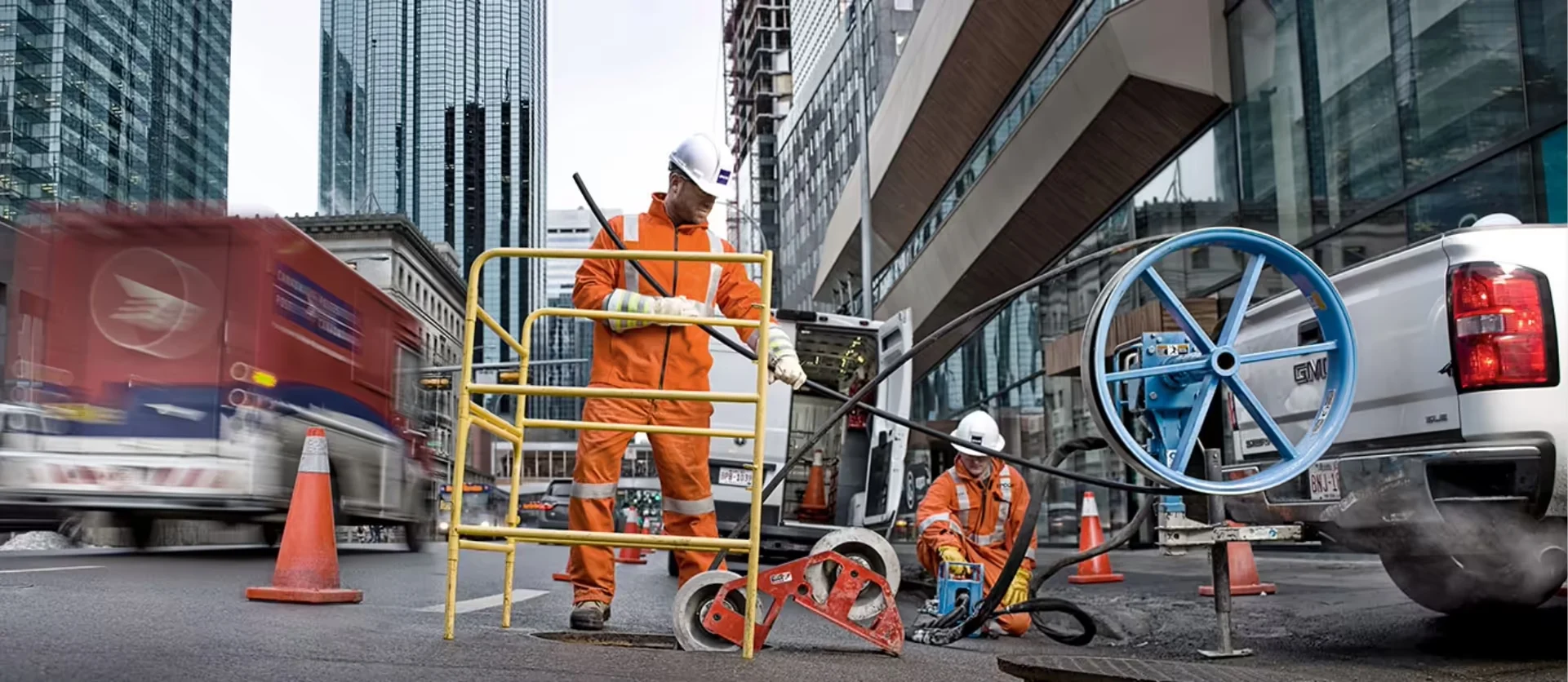 EPCOR technicians using a pulley system and safety guard to perform underground cable work on a city street.