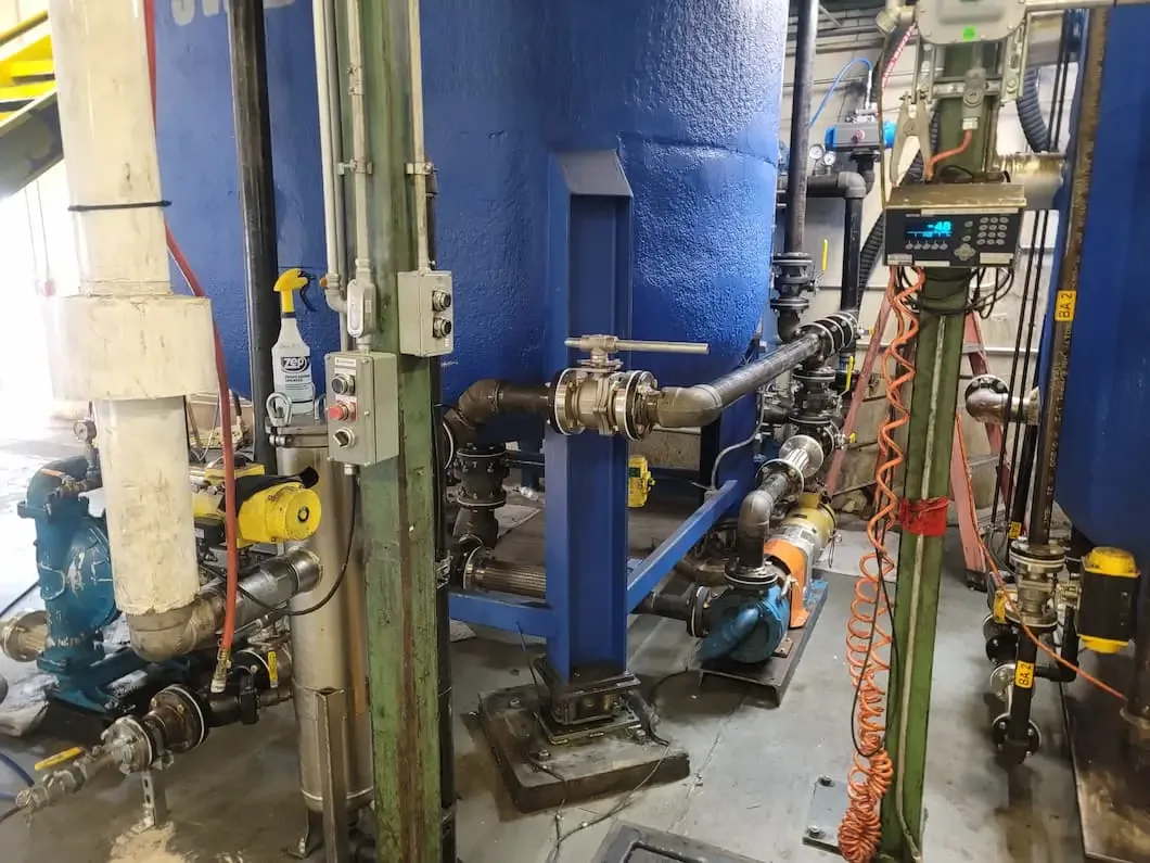 Industrial equipment with blue tanks, pipes, valves, pumps, and a control panel.