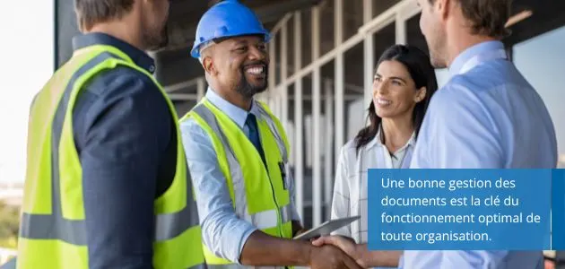 Three professionals, two men and one woman, are gathered on a construction site, smiling and shaking hands.
