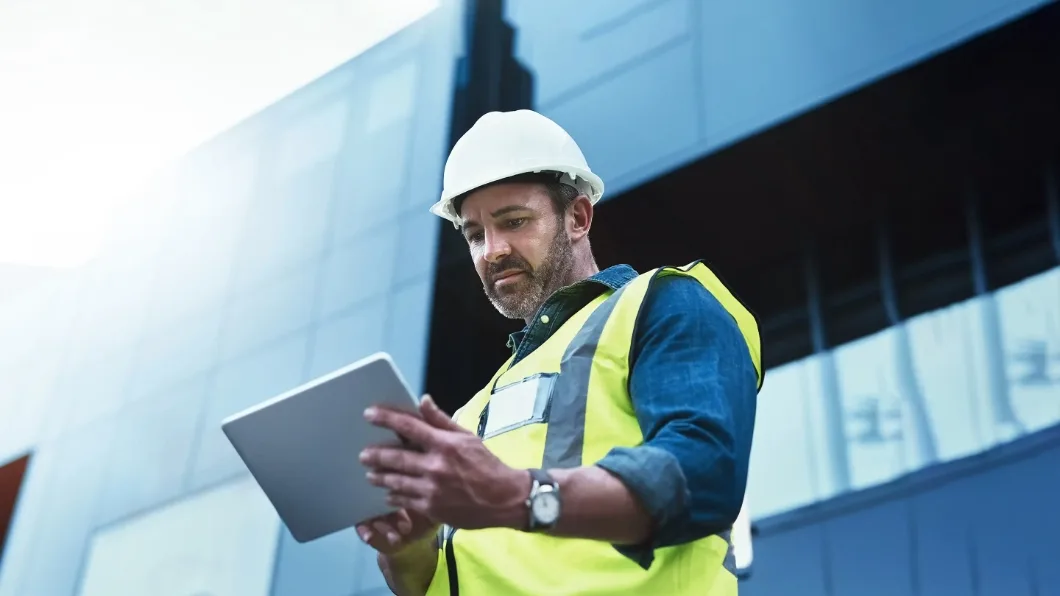  Construction worker in a hard hat and safety vest using a tablet.
