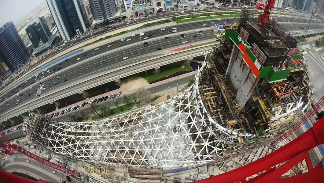 A construction site in Dubai, with a building under construction that has a unique, geodesic dome-like base, and a skyscraper.