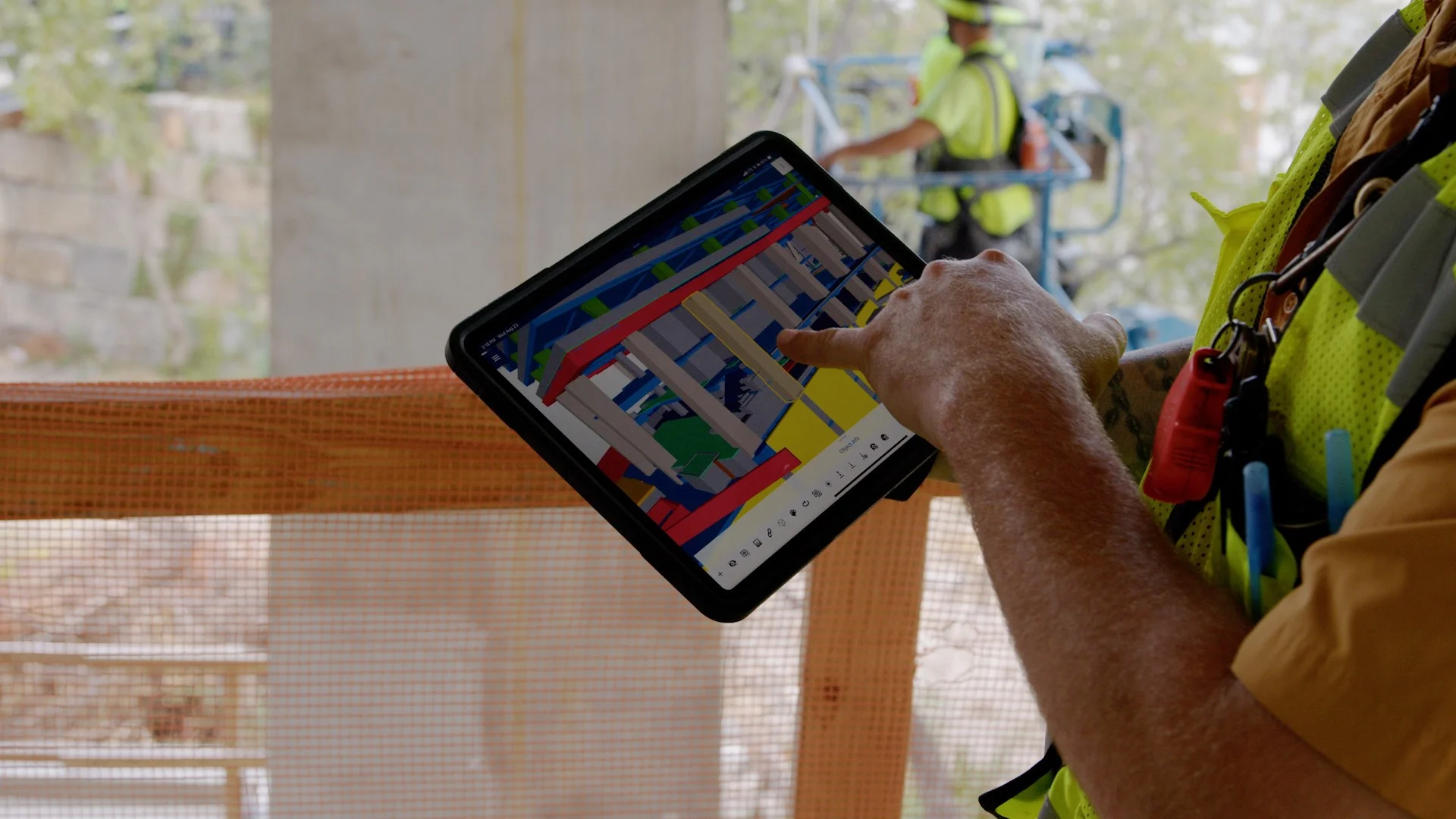 A construction worker uses a tablet to view a 3D model of a building project on site.