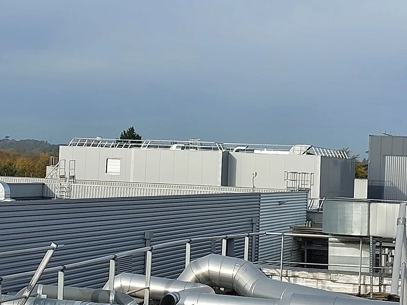 An exterior shot of a modern industrial building with large metal pipes in the foreground and ventilation systems on the roof.