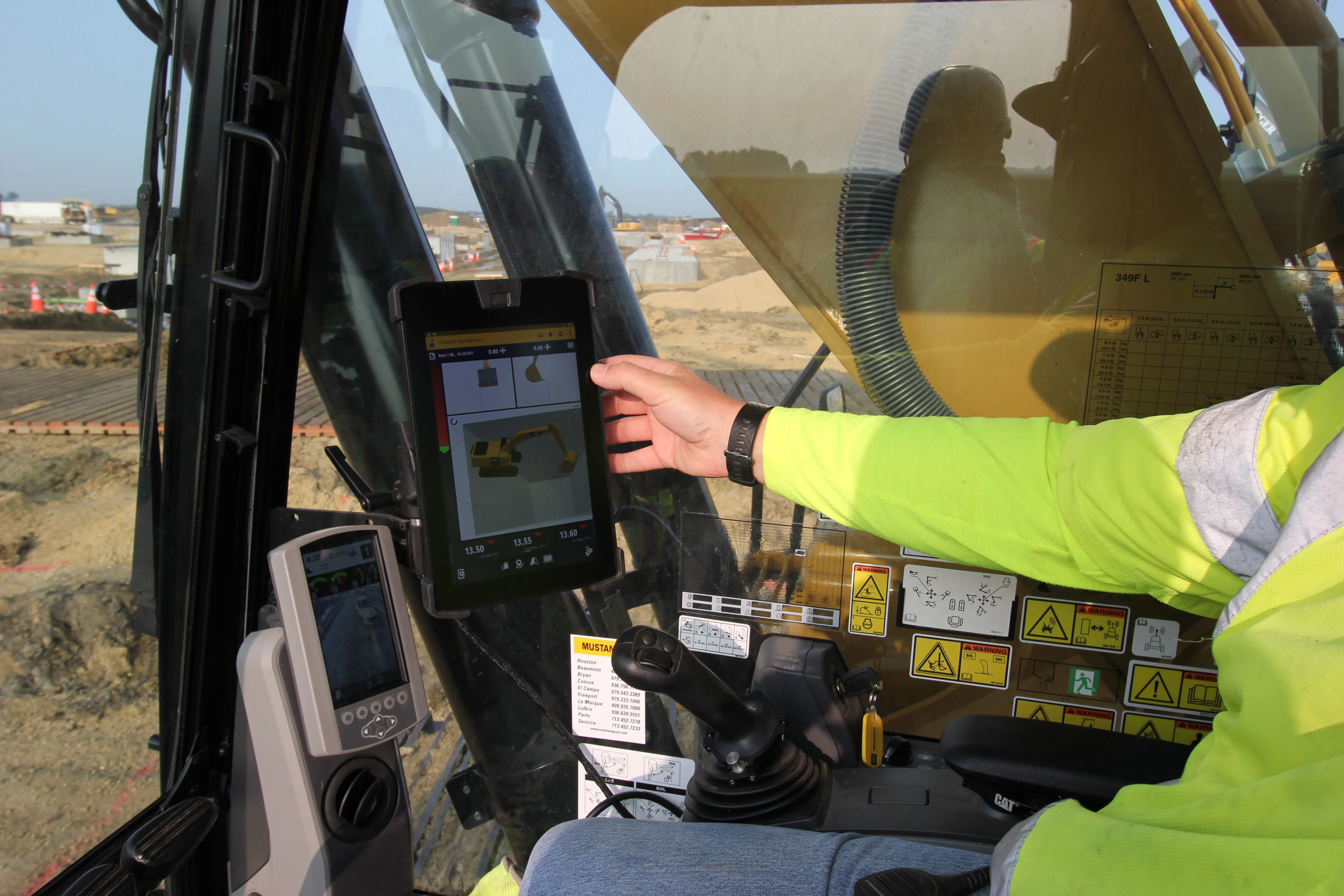 Construction worker in a high-visibility vest operates heavy machinery using a tablet.