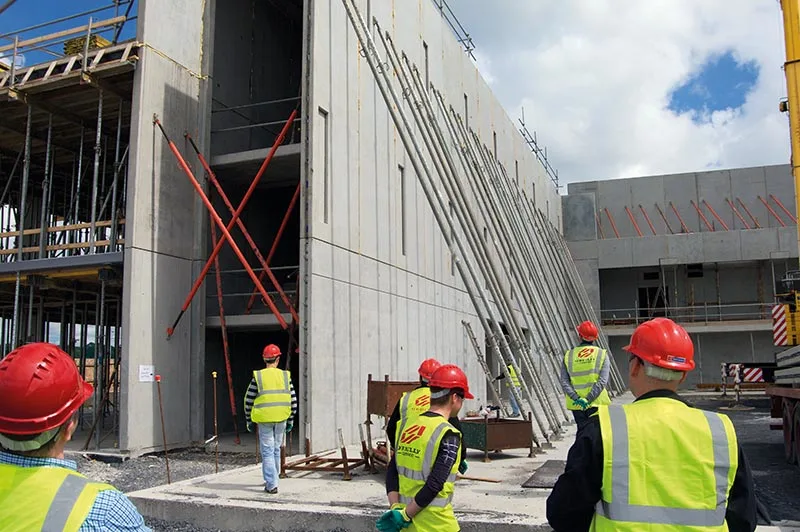 Construction workers in hard hats and high-visibility vests observe the ongoing construction of a concrete building.