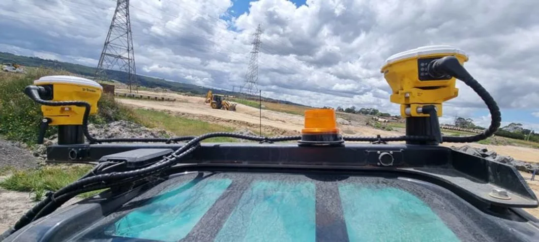 Two yellow GPS units and an orange beacon are mounted on a construction vehicle on a sunny day.