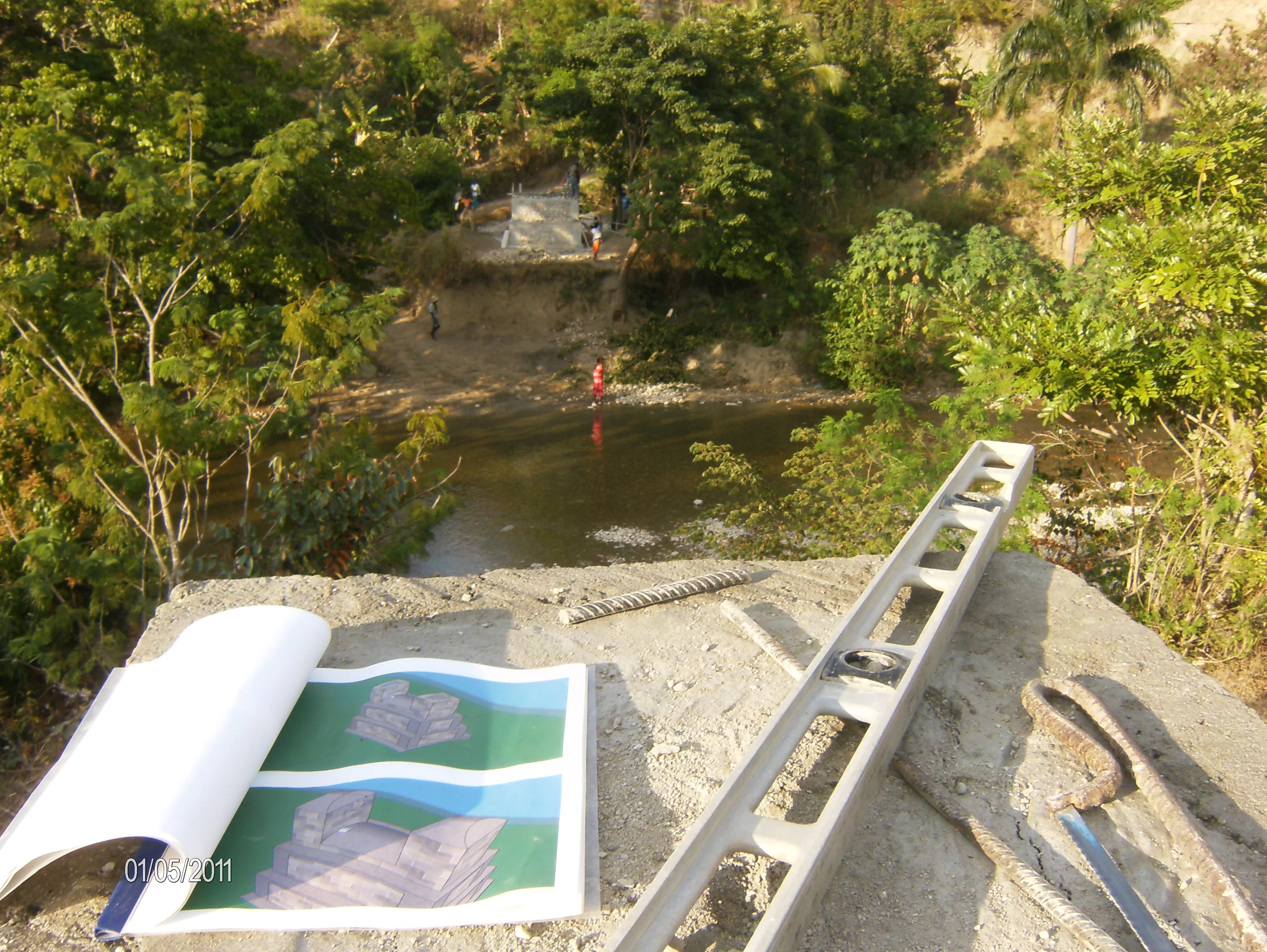 A view of the river from above with a spirit level and 3D visual plans of the bridge on a rock.