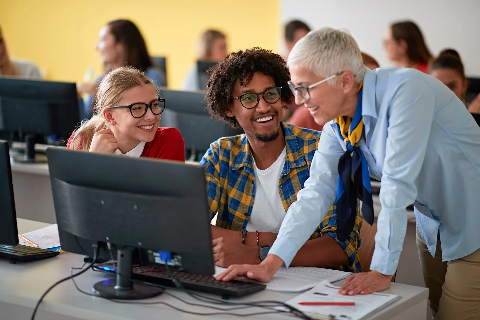 A diverse group of students and a teacher work together on computers in a classroom.