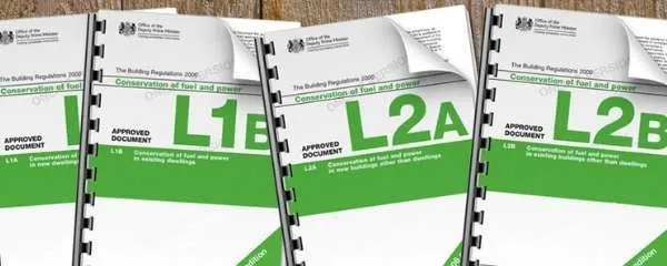 Four spiral-bound UK Building Regulations documents labeled L1A, L1B, L2A, and L2B with green covers on wooden surface.