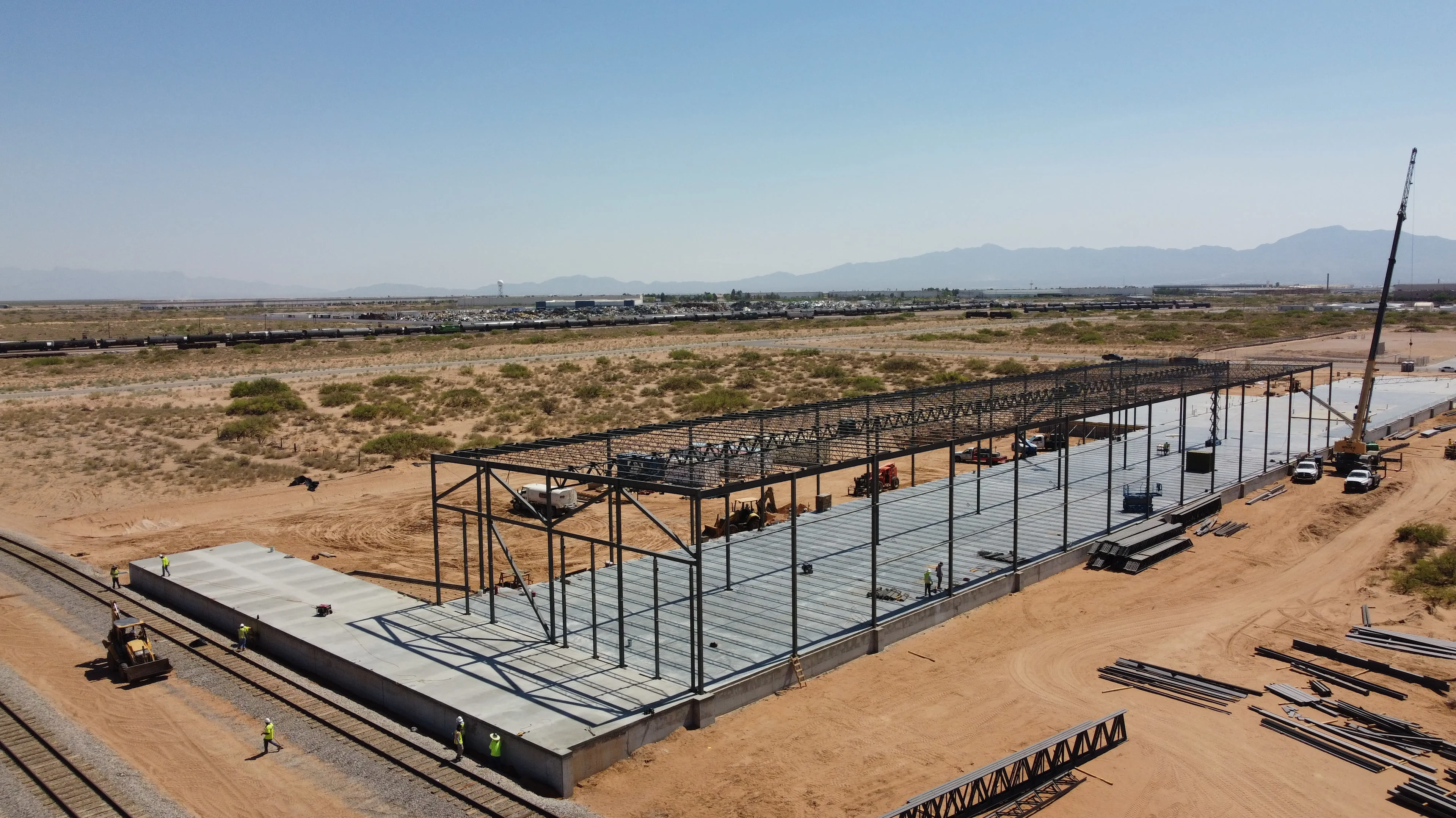 Aerial view of a large industrial building under construction. A crane is visible, along with construction workers and heavy machinery.