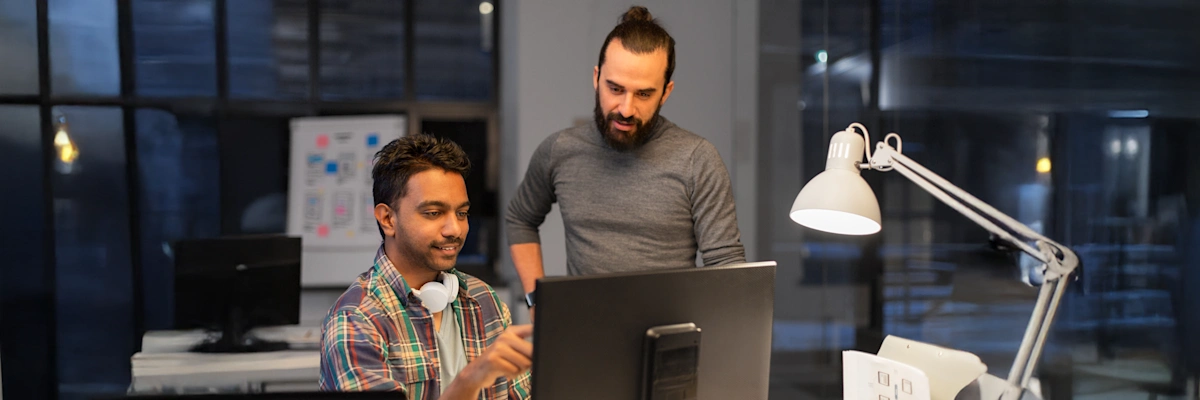Two coworkers collaborating on a BIM project at a computer in a modern office, reviewing building models on screen.