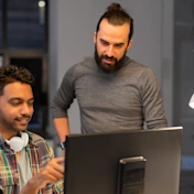 Two coworkers collaborating on a BIM project at a computer in a modern office, reviewing building models on screen.