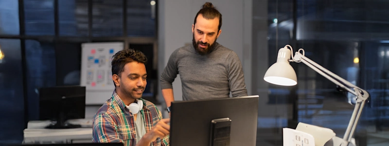 Two coworkers collaborating on a BIM project at a computer in a modern office, reviewing building models on screen.
