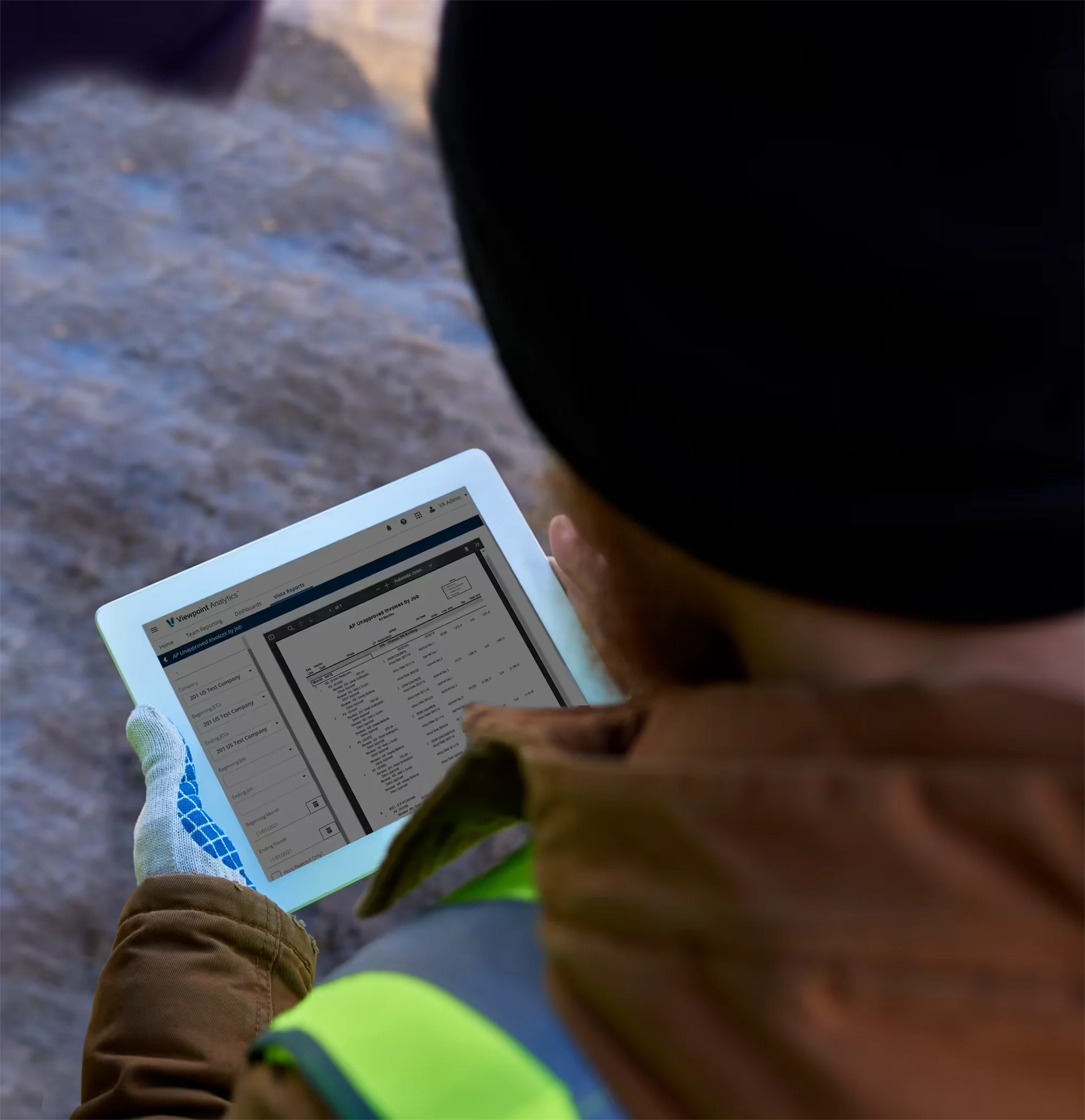 A person in a safety vest and beanie uses a tablet to view data on a screen.
