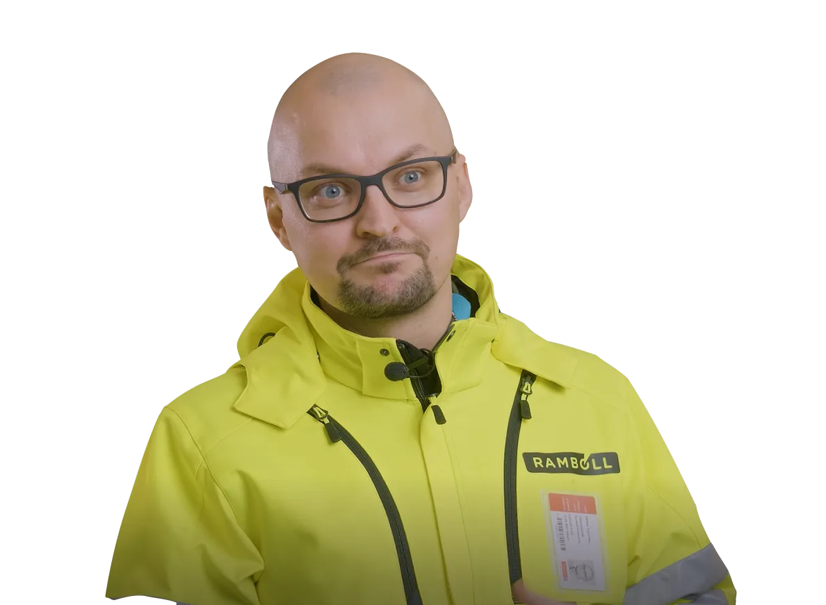 A man wearing a bright yellow jacket with the Ramboll logo on it, along with glasses, looks slightly to the side with a quizzical expression.