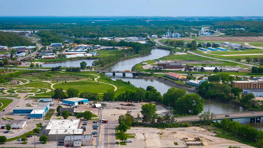 Aerial Norfolk, NE: Elkhorn River, bridges, construction site (aggregate, pipes), blue industrial hangars, grain silos, United Van Lines truck.