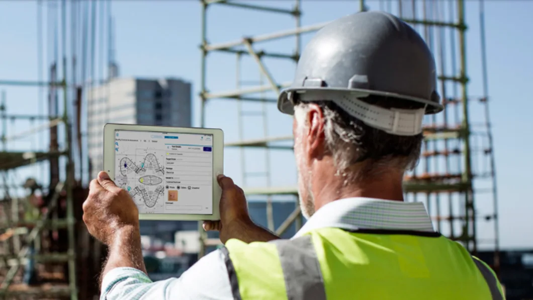 Worker in hard hat and vest using a tablet at a construction site