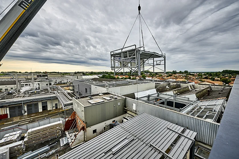 A large steel frame is being lifted by a crane over a construction site.