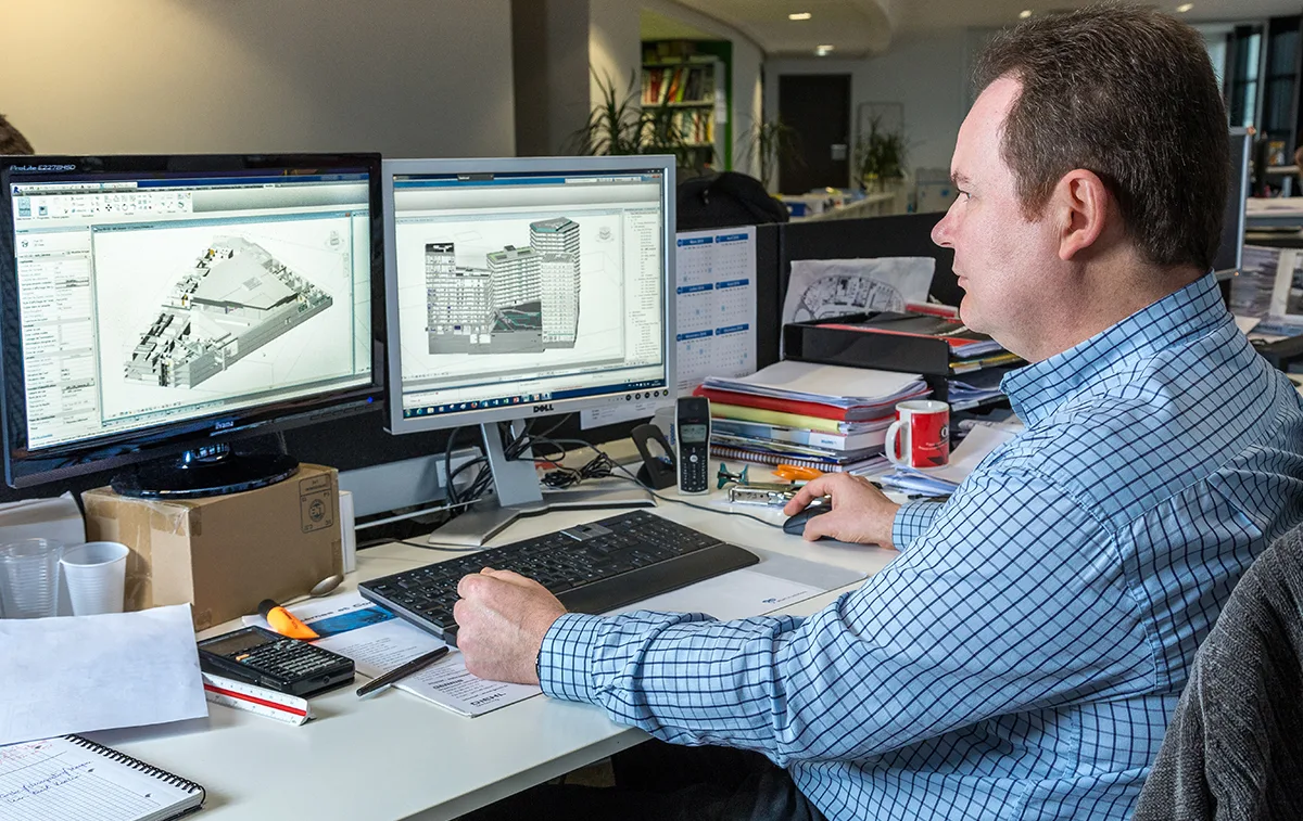 An architect works on his computer, reviewing blueprints on two monitors.